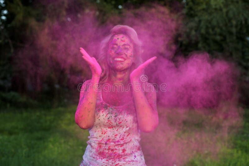 Portrait of positive young model having fun with a cloud of pink dry Holi paint at the park. Portrait of positive young woman having fun with a cloud of pink dry royalty free stock photos